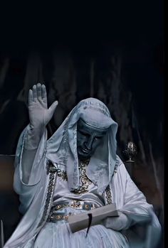 a man dressed in white sitting down with his hands up