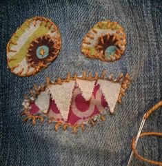 a pair of scissors is cutting through the hole in jeans with embroidered eyes and teeth