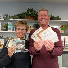 a man and woman holding up some cards in front of a shelf with books on it