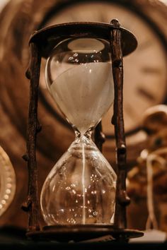 an old - fashioned hourglass with sand running through it and a clock in the background