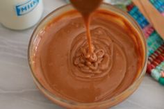 a glass bowl filled with chocolate frosting next to a bottle of milk