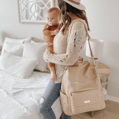 a woman holding a baby in her arms while wearing a hat and carrying a purse