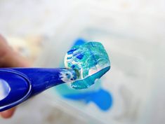 a person holding a toothbrush with blue and white paint on it's handle