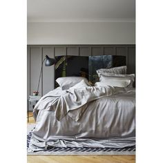 a bed with white sheets and pillows in a bedroom next to a wall mounted lamp