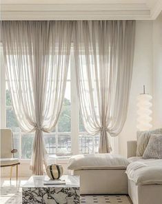 a living room filled with white furniture and windows covered in sheer draping curtains