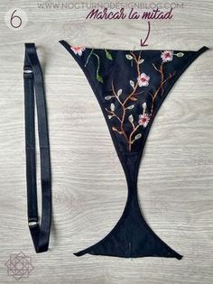 the back side of a black bag with embroidered flowers on it, and an attached strap