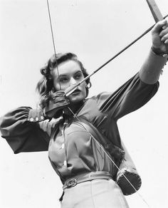 an old photo of a woman with a bow and arrow in her hands, holding onto the strings