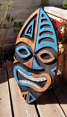 a blue and brown mask sitting on top of a wooden table next to flowers in a pot