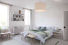 a bedroom with a bed, chair, and table in front of two large windows