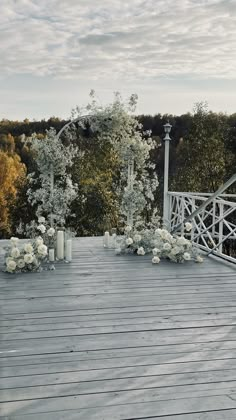 an outdoor wedding setup with white flowers and candles on the deck, surrounded by trees