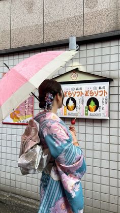 a woman walking down the street with an umbrella over her head, in front of a wall