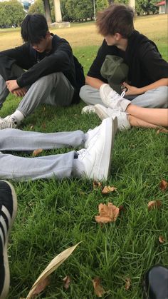 three young men sitting on the grass with their feet crossed