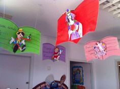 several colorful kites hanging from the ceiling in a room filled with children's artwork