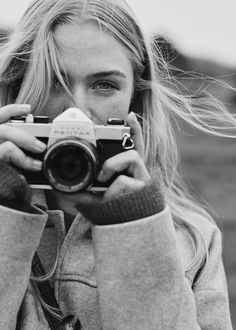 a black and white photo of a woman holding a camera in front of her face