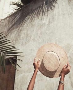 a person holding up a straw hat in front of a palm tree