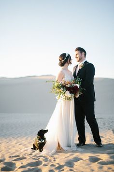 a bride and groom standing in the sand with their dog