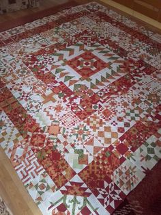 a red and white quilt is laying on the floor in front of a wooden table