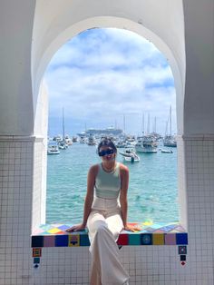 a woman sitting on top of a bench next to the ocean with boats in the water