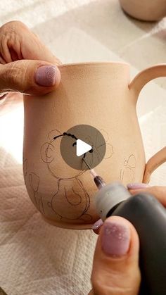 a woman is painting a mug with an animal on it's side and has her thumb in the cup