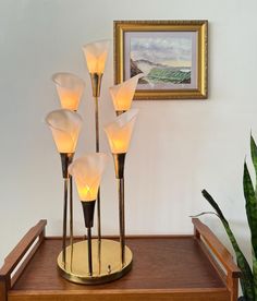 five lights on a wooden table in front of a painting and potted plant,