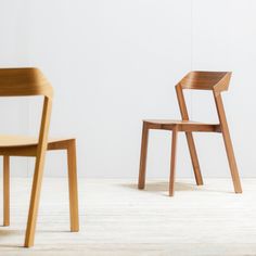 two wooden chairs sitting next to each other on top of a hard wood floor in front of a white wall