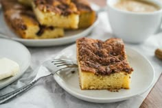 a piece of cake sitting on top of a white plate next to a cup of coffee