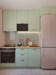 a kitchen with light green cabinets and white tile flooring on the walls, along with a pink refrigerator freezer