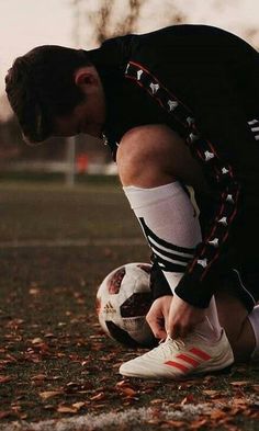 a young man kneeling down with a soccer ball in his hand while wearing adidas socks