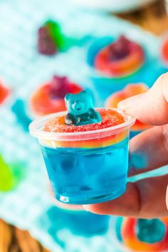 a hand holding a small cup filled with blue liquid and a gummy bear on top