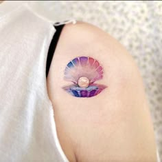 a woman with a tattoo on her shoulder has a shell in the shape of a pearl