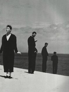 a group of people standing on top of a beach next to the ocean and one person holding a cell phone