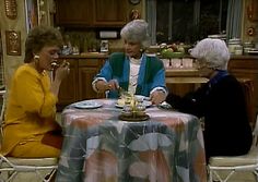 two women sitting at a table with plates and cups in front of them, talking