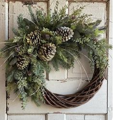 a wreath with pine cones and greenery hanging on a door