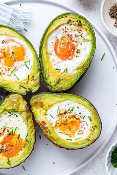 four avocados with eggs in them on a white plate next to other dishes