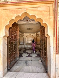 a woman in a pink dress is standing at the entrance to a building with ornate doors