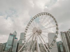 a ferris wheel in the middle of a city with tall buildings and cloudy skies behind it