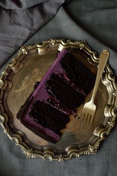 a piece of chocolate cake on a silver plate with a fork and knife next to it