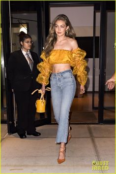 a woman in yellow top and jeans walking out of a building with her handbag