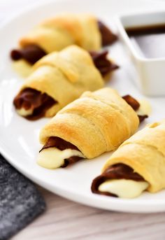 three croissants on a white plate with dipping sauce