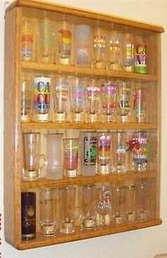 a wooden shelf filled with lots of glasses on top of a white wall next to a chair