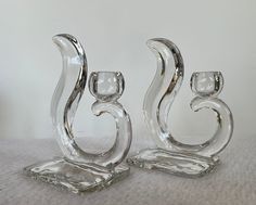 two clear glass candlesticks sitting next to each other on a white tablecloth