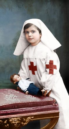 a young boy dressed as a nurse with a doll on top of a chair in front of a painting