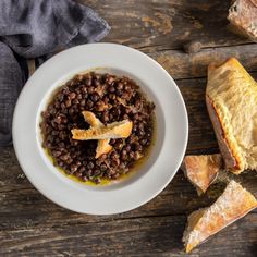 a white bowl filled with beans next to bread on top of a wooden table,