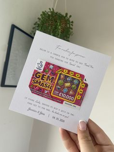 a person holding up a card with some candy on it in their left hand and a potted plant behind them