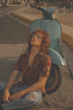 a woman sitting on the ground next to a scooter with her eyes closed