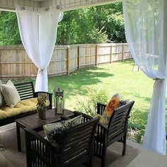 a covered patio with couches, tables and curtains on the outside side of it