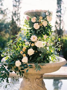 a water fountain with flowers growing out of it's sides and greenery on top