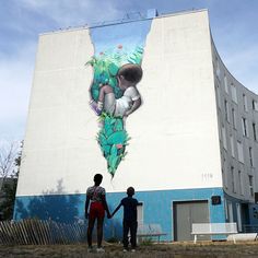 two people standing in front of a large mural on the side of a building