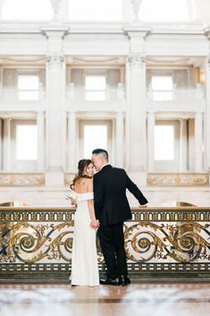 a bride and groom standing in front of a balcony at the state capitol building during their wedding day