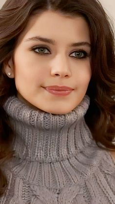 a woman with brown hair wearing a gray turtle neck sweater